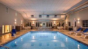 Une piscine intérieure avec un sol carrelé, un poste de surveillance pour le sauveteur et des chaises longues.