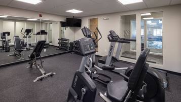 A gym with cardio machines, weight benches, and dumbbells.