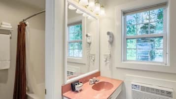 A bathroom with a large mirror, a pink sink, a hairdryer, and a window with a view of trees.