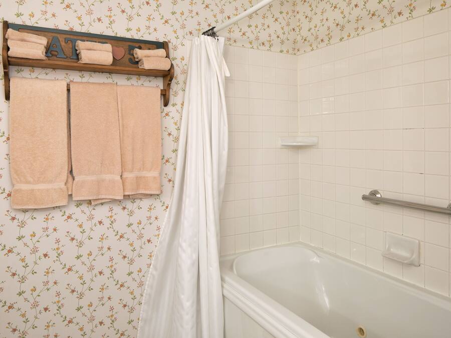 A bathroom with a bathtub, a shower curtain, and a towel rack with folded towels.
