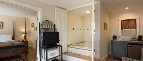 A bedroom with a bed, a TV, a microwave, a small table, and a window with curtains.