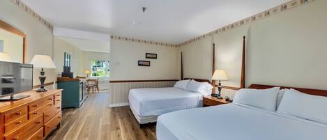 A hotel room with two beds, a wooden dresser, a desk with a lamp, and a view of the outside.