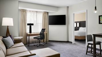 Quarto de hotel com sofá, escrivaninha com cadeira, televisão e cama.