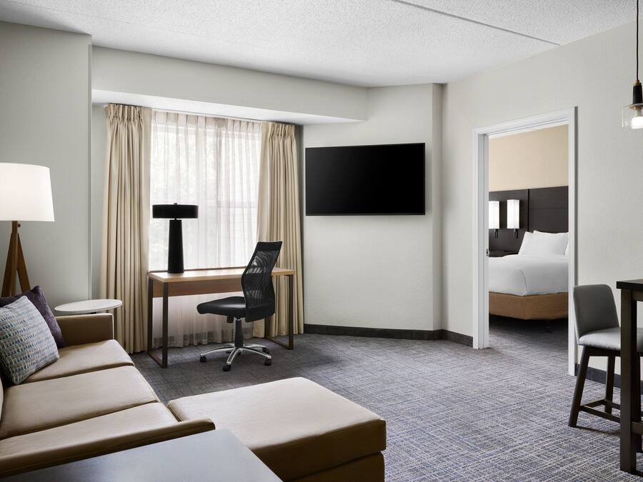 Quarto de hotel com sofá, escrivaninha com cadeira, televisão e cama.