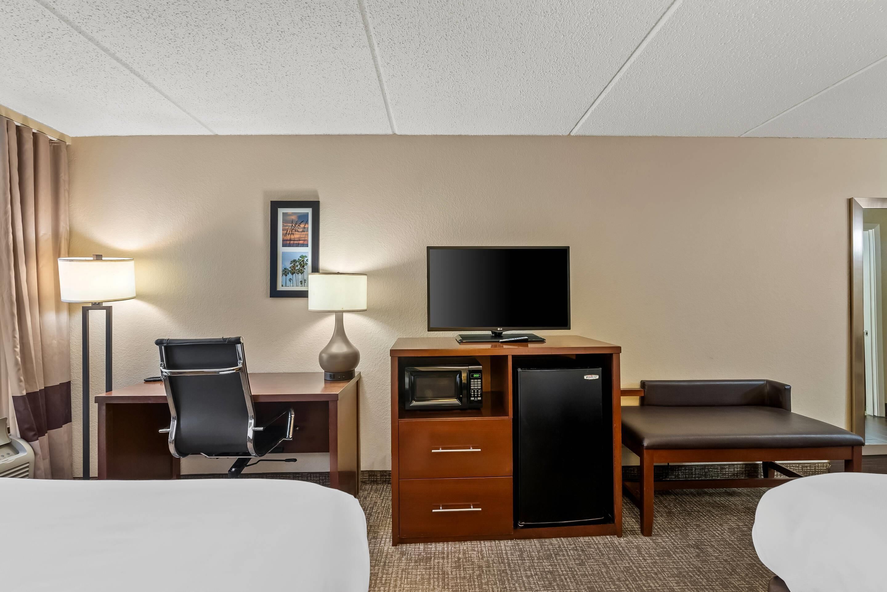A hotel room with a bed, a desk with a chair, a television, a refrigerator, and a microwave.