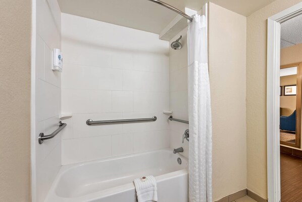 A bathroom with a white bathtub, grab bars, and a shower curtain.