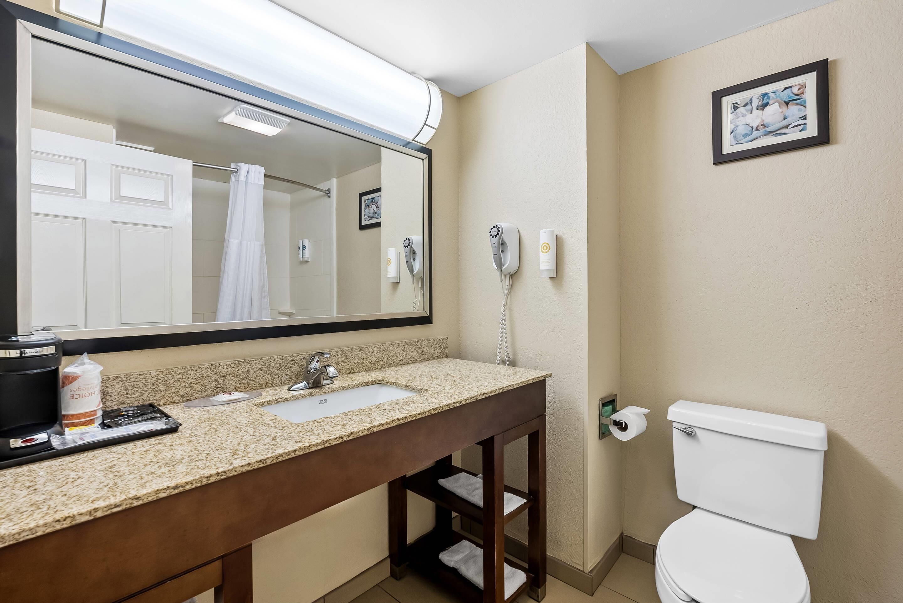 A bathroom with a double sink, a mirror, a toilet, and a hairdryer on the wall.