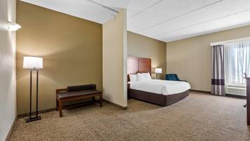 Una habitación de hotel con cama, mesita de noche, lámpara y un banco.