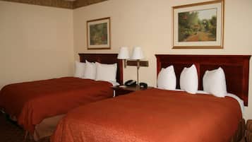 Habitación de hotel con dos camas, una mesita de noche con lámpara y dos cuadros en la pared.