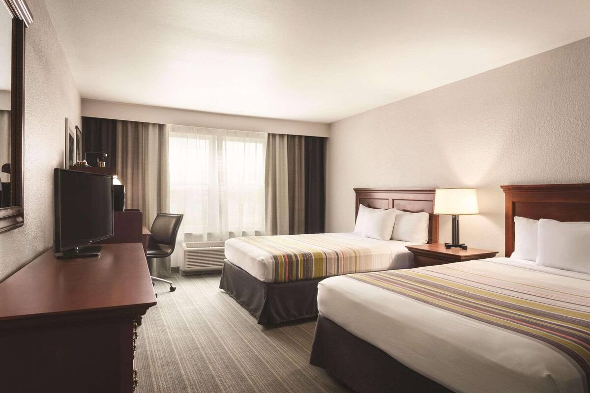 A hotel room with two beds, a desk, a television, and a window with curtains.