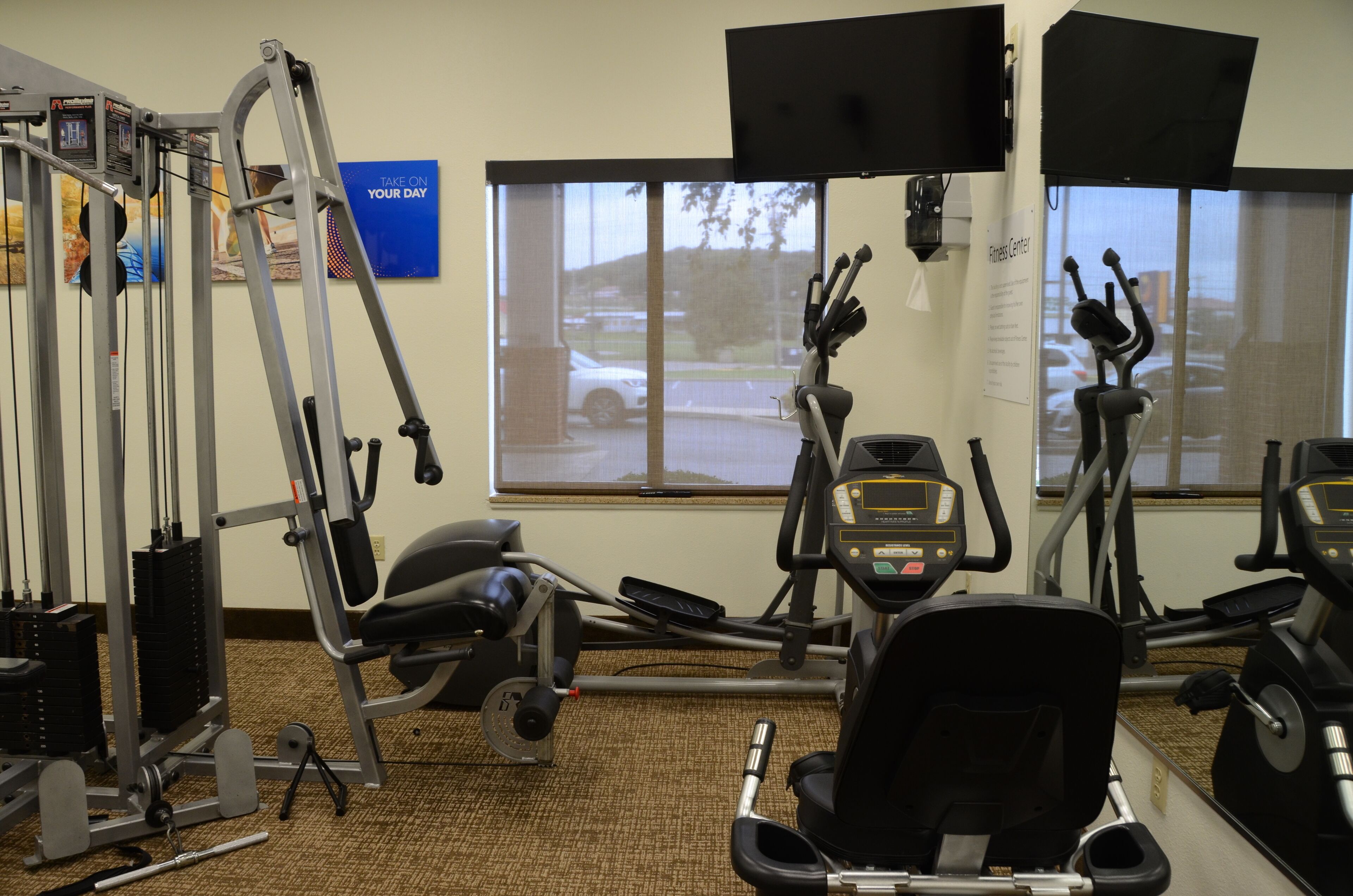 A gym with various exercise equipment, a large window, and a motivational poster on the wall.
