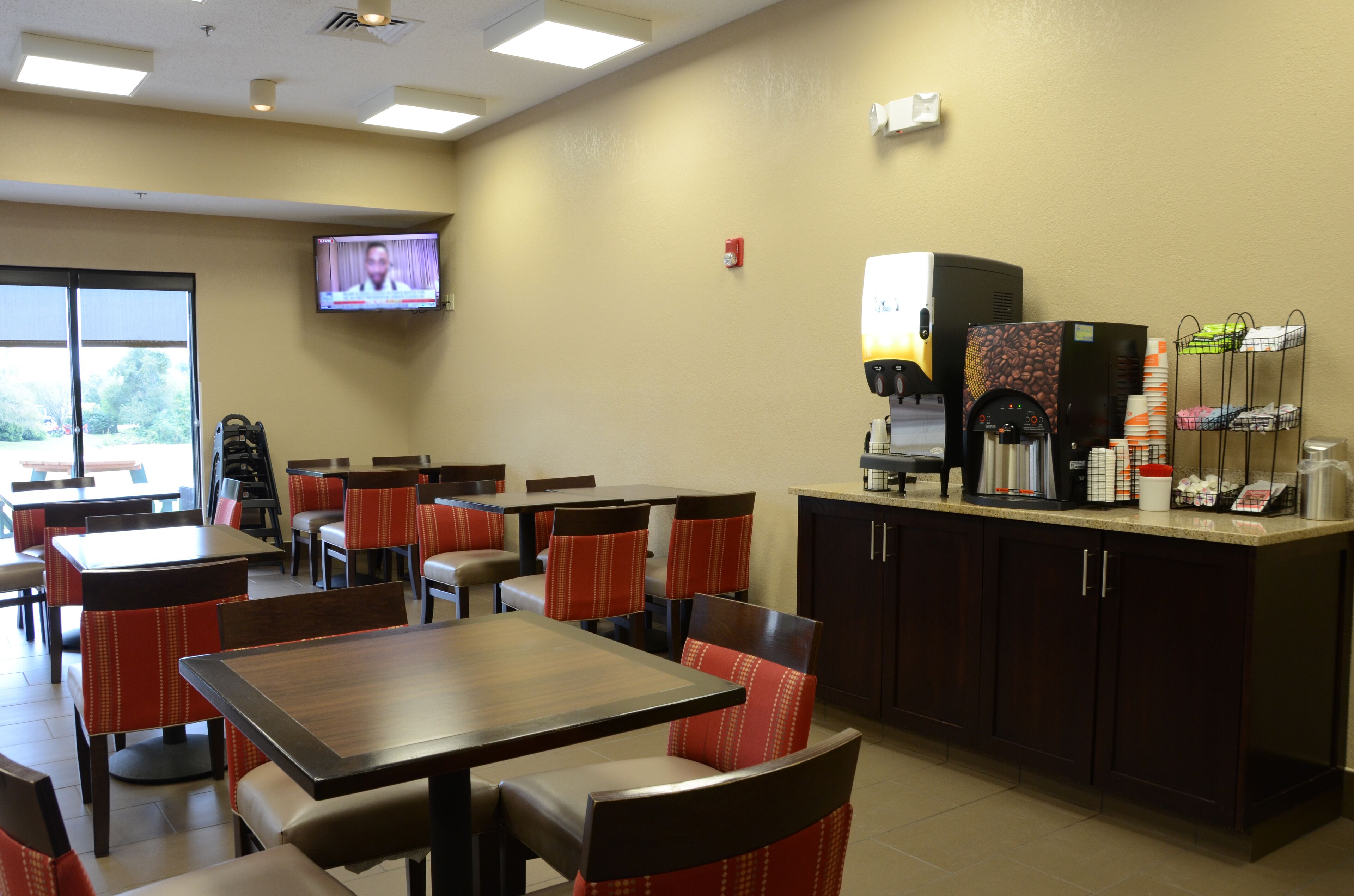 A restaurant with tables and chairs, a coffee machine, and a television on the wall.