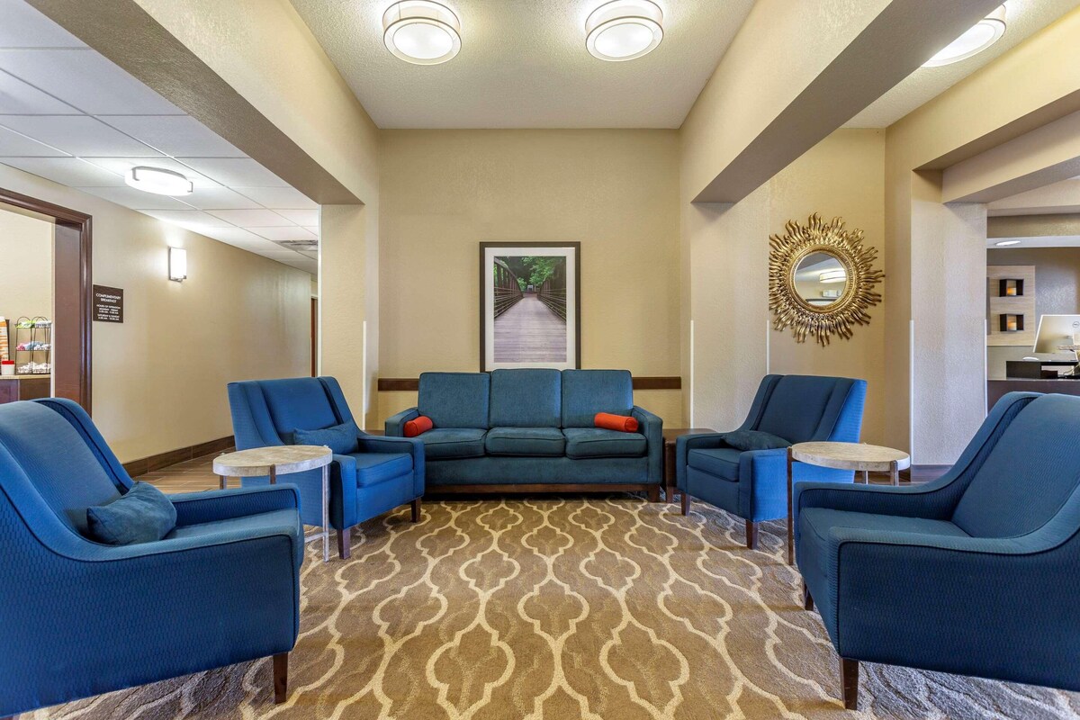 A hotel lobby with a seating area featuring blue armchairs and a sofa, a patterned carpet, and a framed picture on the wall.