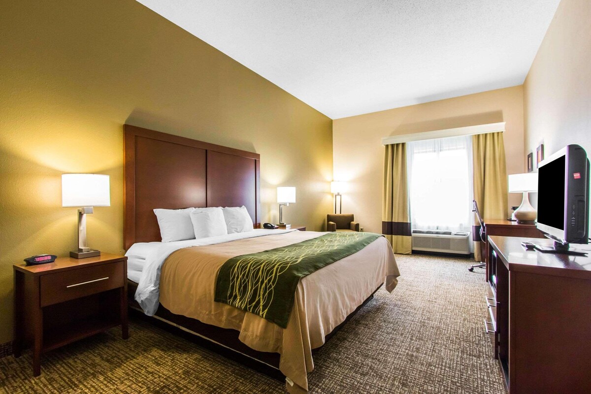 A hotel room with a bed, bedside tables, lamps, a TV, and a desk.