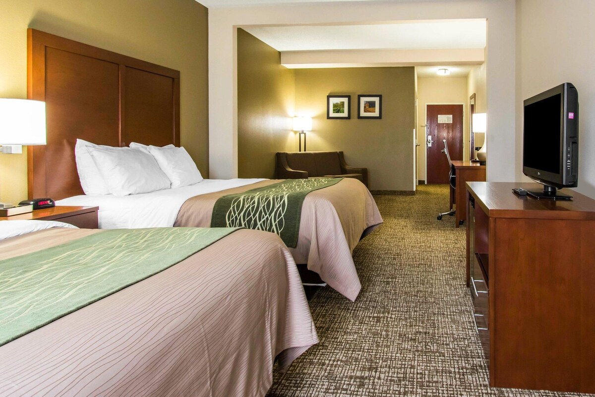 A hotel room with two beds, a desk with a television, a lamp, and a door leading to a hallway.