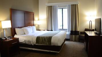 Habitación de hotel con una cama grande, dos mesitas de noche, un escritorio, una silla y una ventana con cortinas.