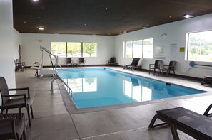 A swimming pool with a pool ladder, lounge chairs, and a view of trees through large windows. - Comfort Inn & Suites Cave City (Cave City)