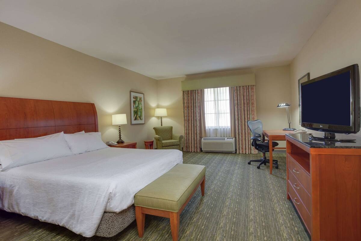 Habitación de hotel con una cama grande, un escritorio con computadora, una silla, televisor y aire acondicionado.