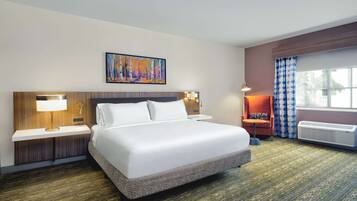 Habitación de hotel con una cama grande, una mesita de noche con lámpara, una obra de arte en la pared, una ventana con cortinas y un equipo de aire acondicionado.