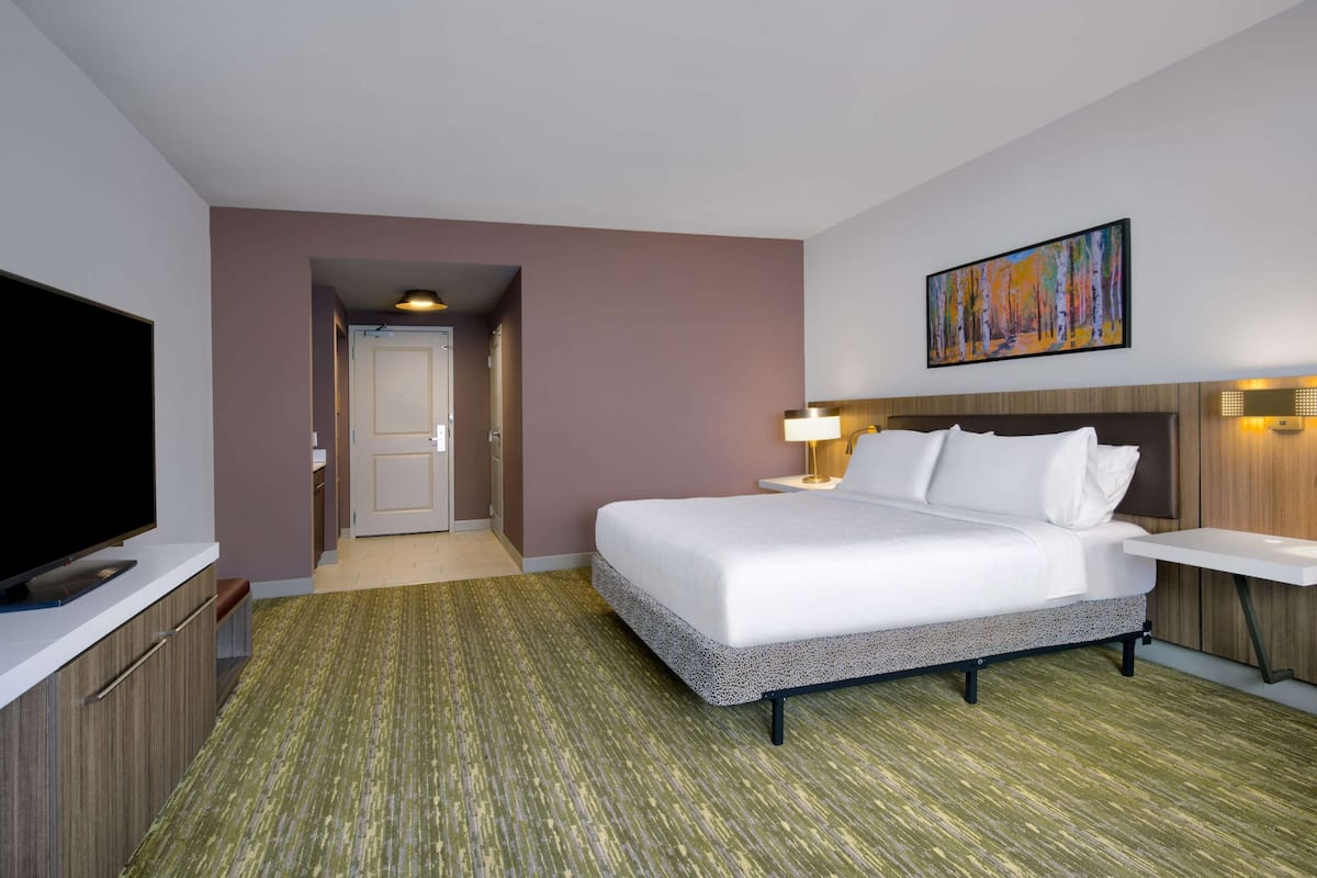 A hotel room with a bed, a TV, a desk, and a painting on the wall.