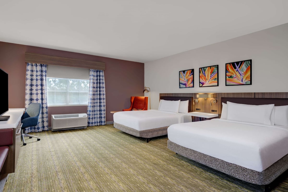 A hotel room with two beds, a desk, a chair, a TV, and a window with curtains.
