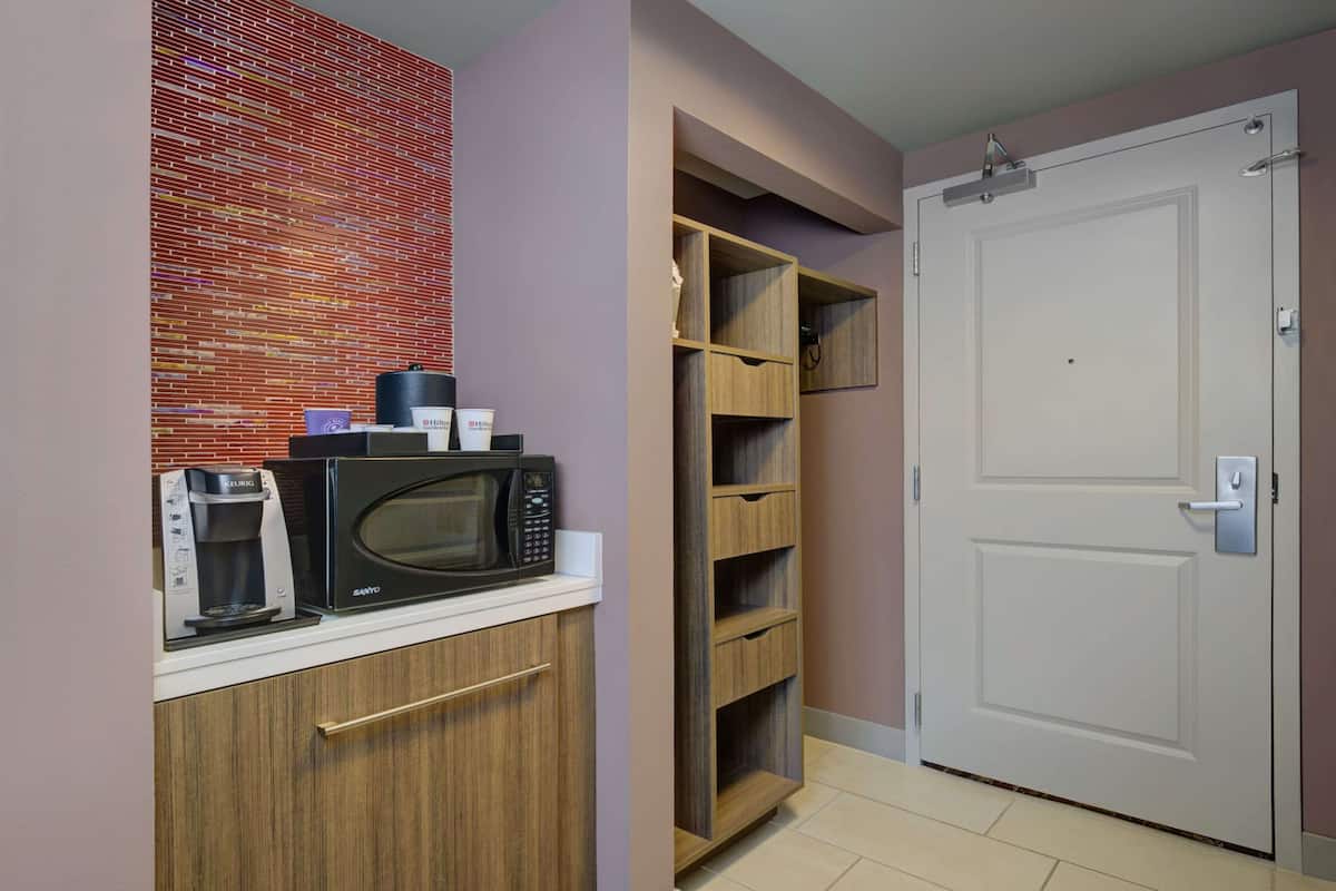 A compact kitchen with a microwave, coffee maker, and wooden shelves.
