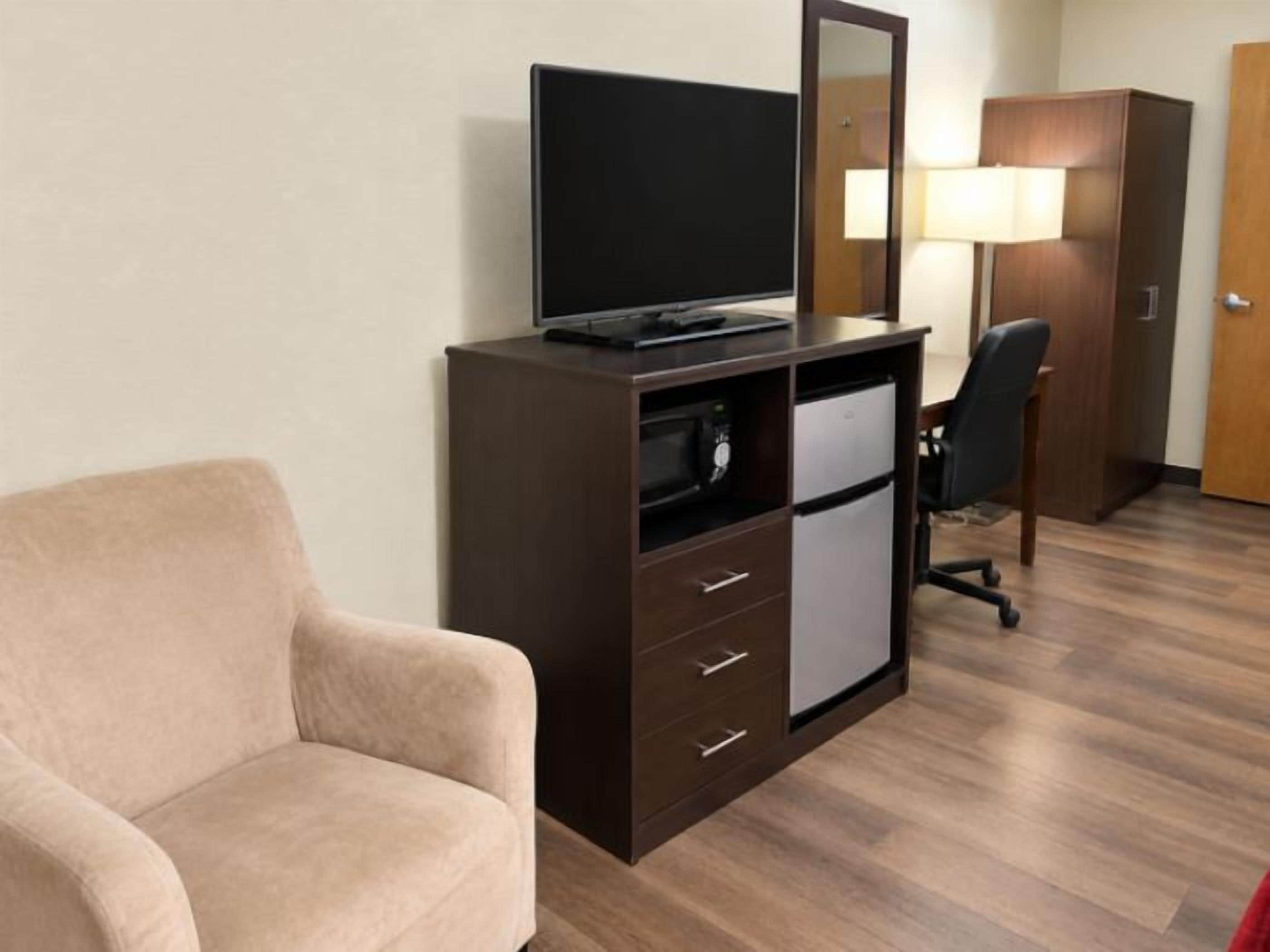 A hotel room with a bed, a desk with a computer, a chair, a television, and a wardrobe.