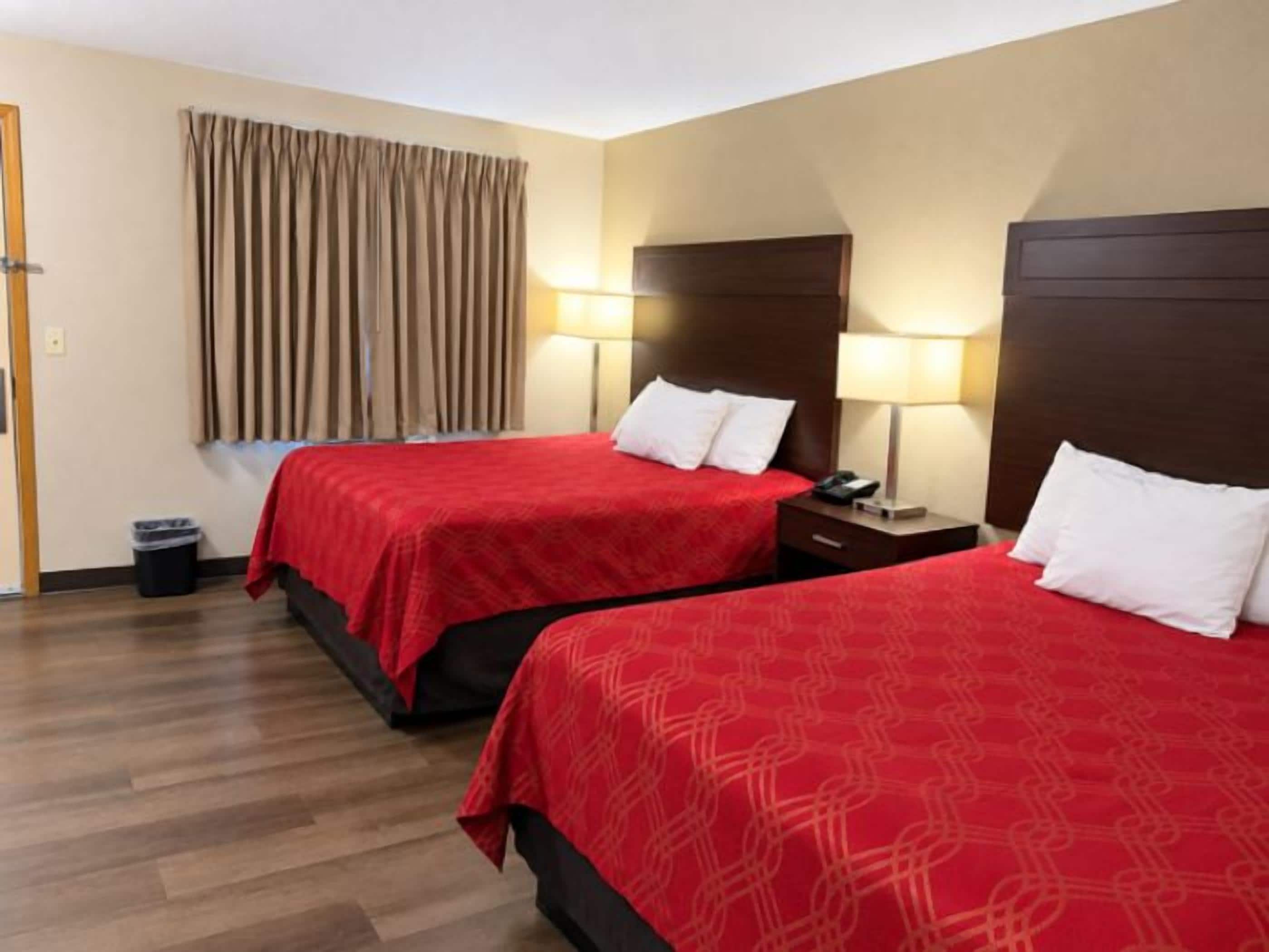 A hotel room with two beds, wooden flooring, a curtain, and bedside lamps.