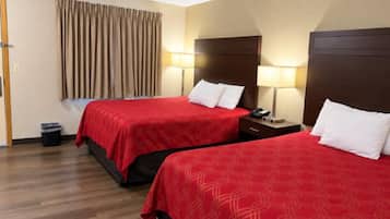 A hotel room with two beds, wooden flooring, a curtain, and bedside lamps.