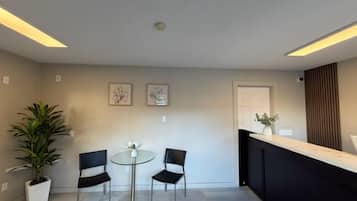 A modern reception area with a glass table, two chairs, a potted plant, and framed artwork on the wall.