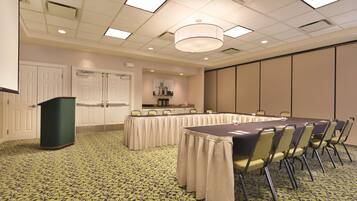 A conference room with a long table, chairs, a podium, and a patterned carpet.