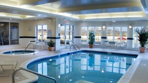 An indoor swimming pool with clear water, surrounded by lounge chairs and potted plants.