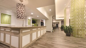 A reception area with a wooden reception desk, a patterned hanging light fixture, and green decorative panels on the walls.