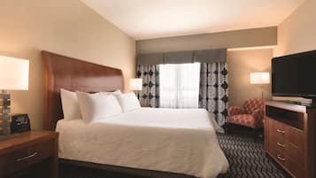 A hotel room with a large bed, two bedside tables with lamps, a TV, a chair, and a window with patterned curtains.