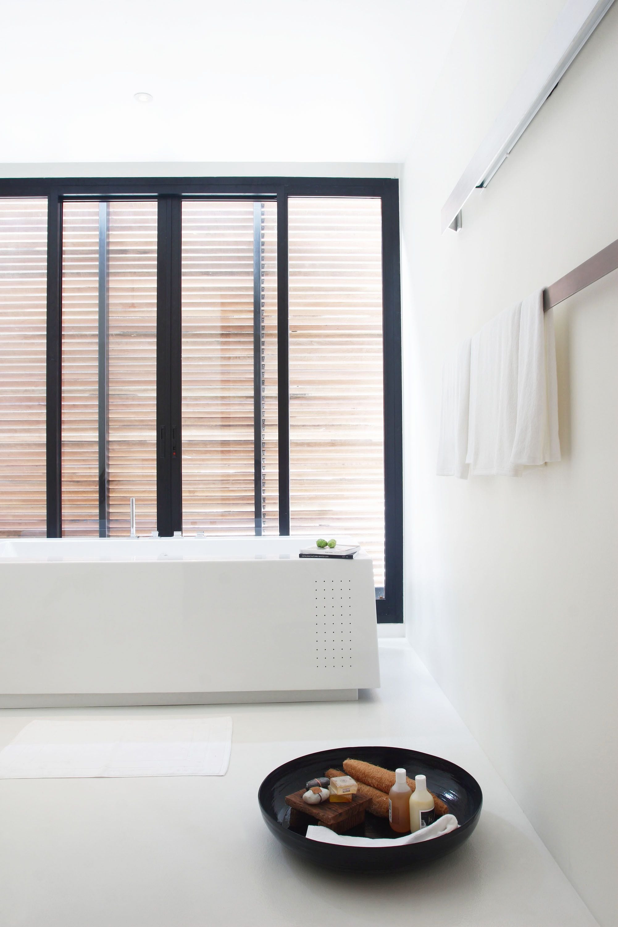 A minimalist bathroom with a large window, a white bathtub, and a black basin with toiletries.