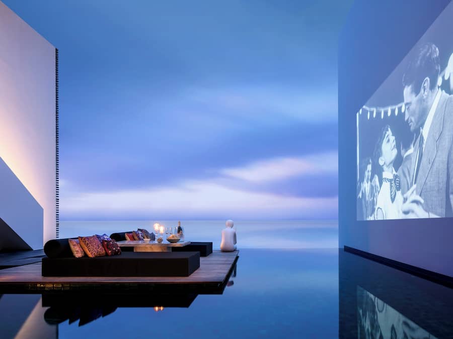 A serene outdoor seating area with a table set for two, overlooking a calm body of water.
