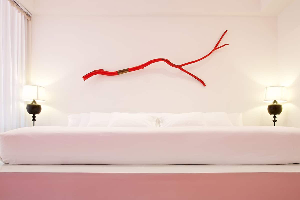 A bedroom with a white bed, two bedside lamps, and a red branch decoration on the wall.