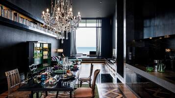 A modern dining area with a chandelier, a view to the sea, and a bar area with a marble countertop.