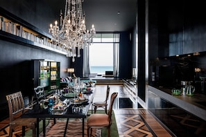 Un comedor moderno con candelabro, vista al mar y zona de bar con encimera de mármol.