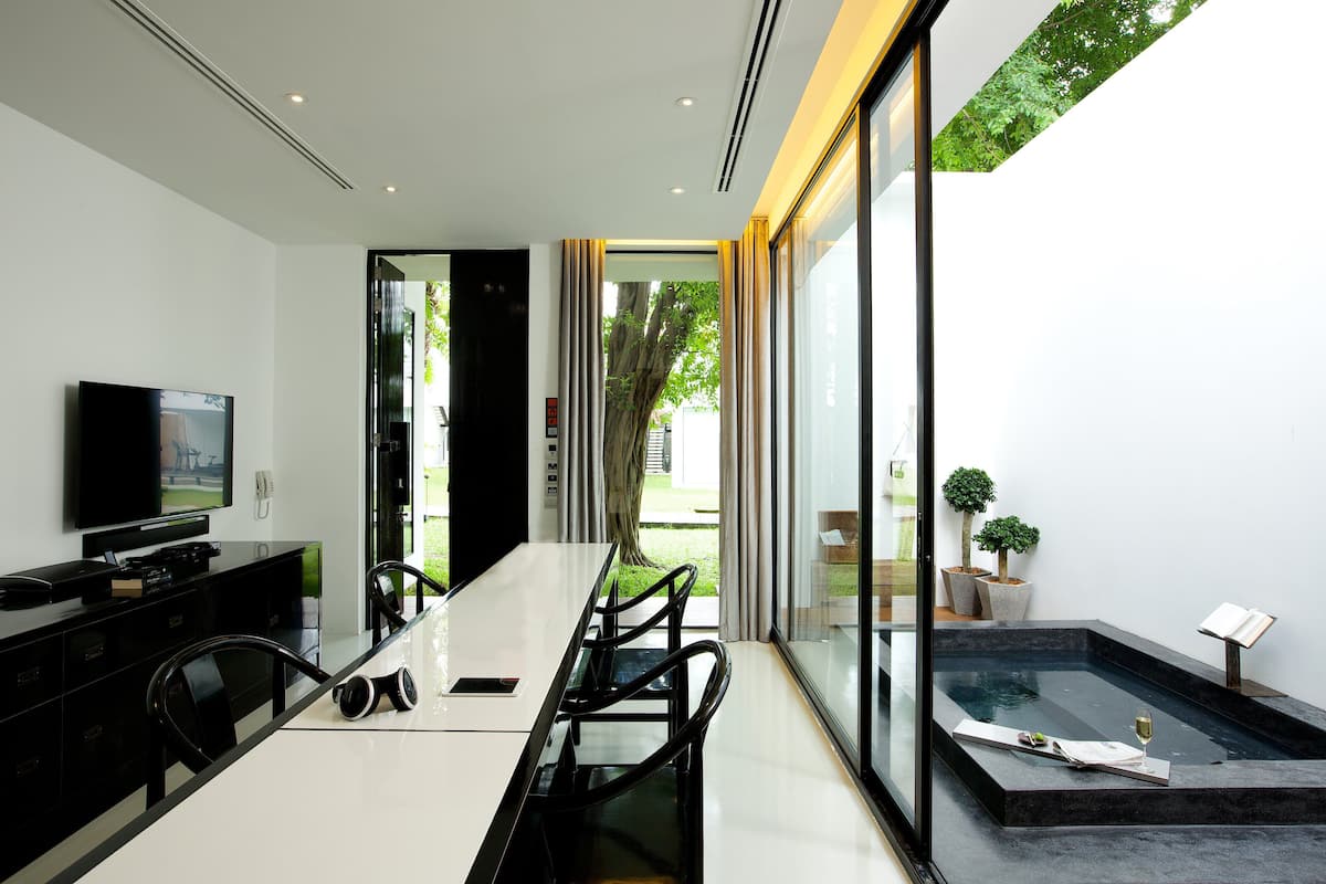A modern dining area with a long table, chairs, a television, and a small indoor water feature.