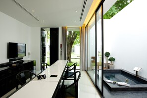 A modern dining area with a long table, chairs, a television, and a small indoor water feature.