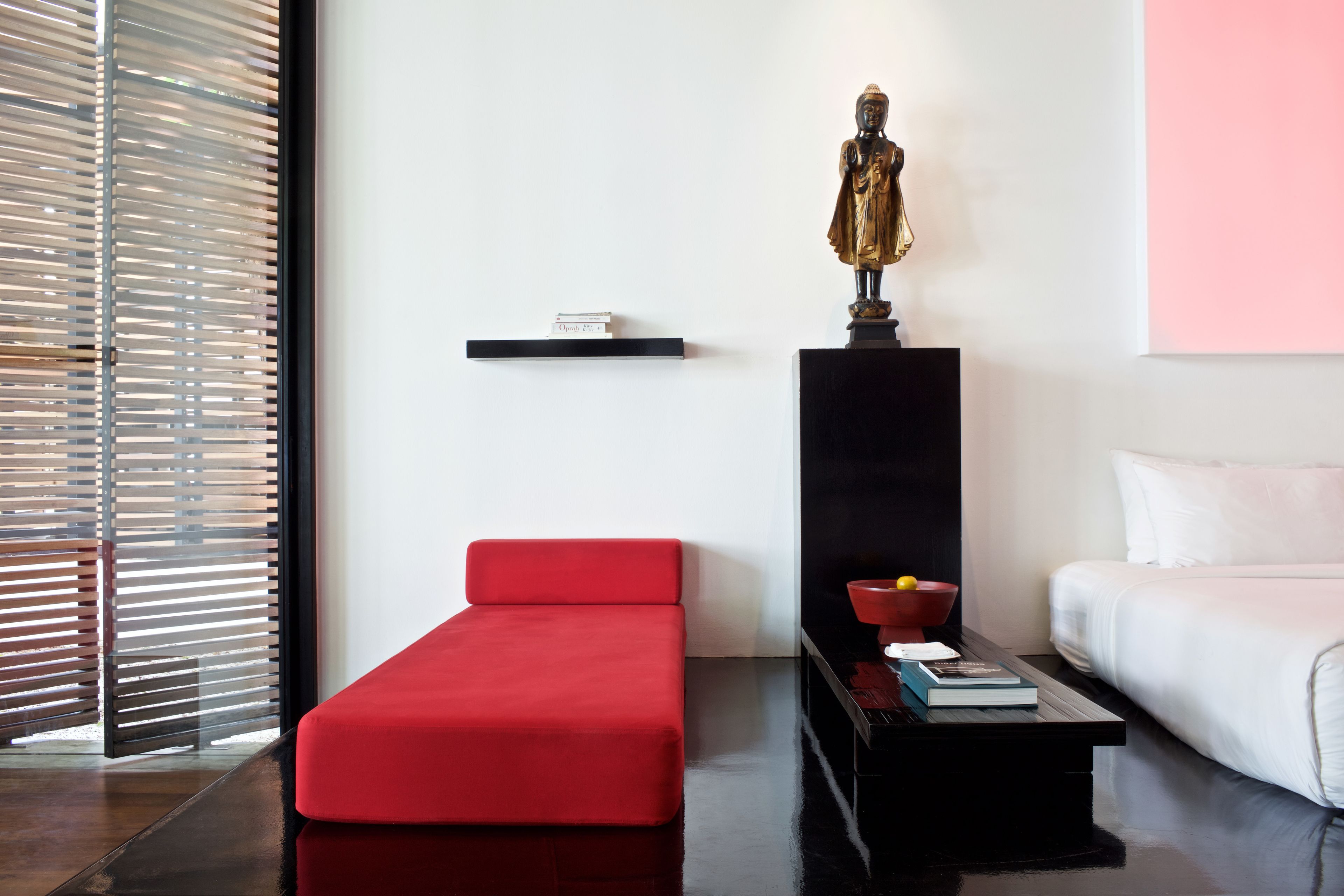 A modern room with a red sofa, a white bed, a black nightstand, and a statue on a pedestal.