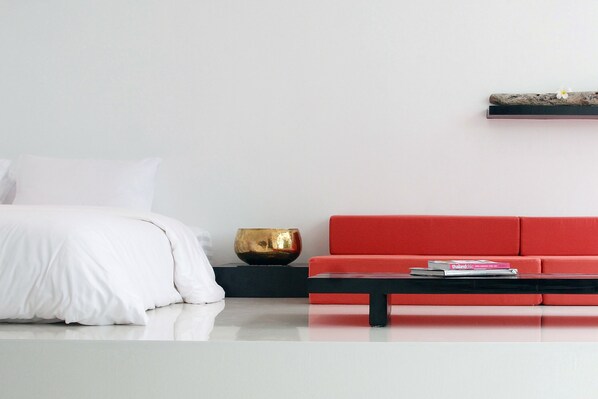 A modern bedroom with a white bed, a red sofa, a black coffee table, and a gold bowl on a black side table.