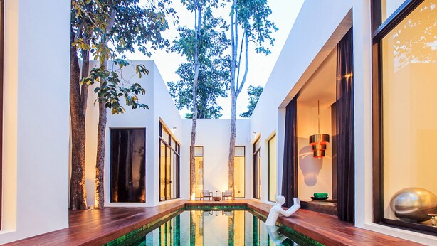 A modern indoor swimming pool with a glass bottom, surrounded by white walls and wooden decks. - The Library (Koh Samui)