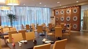 A hotel dining area with tables and chairs, a large window with curtains, and a wall with circular patterns. - Jinjiang Inn ChengDu Wenshufang (Chengdu)