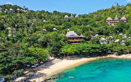 A coastal resort with multiple bungalow-style buildings, a sandy beach, and clear turquoise waters.