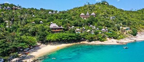 Un resort costero con varias construcciones tipo bungalow, una playa de arena y aguas turquesas cristalinas.