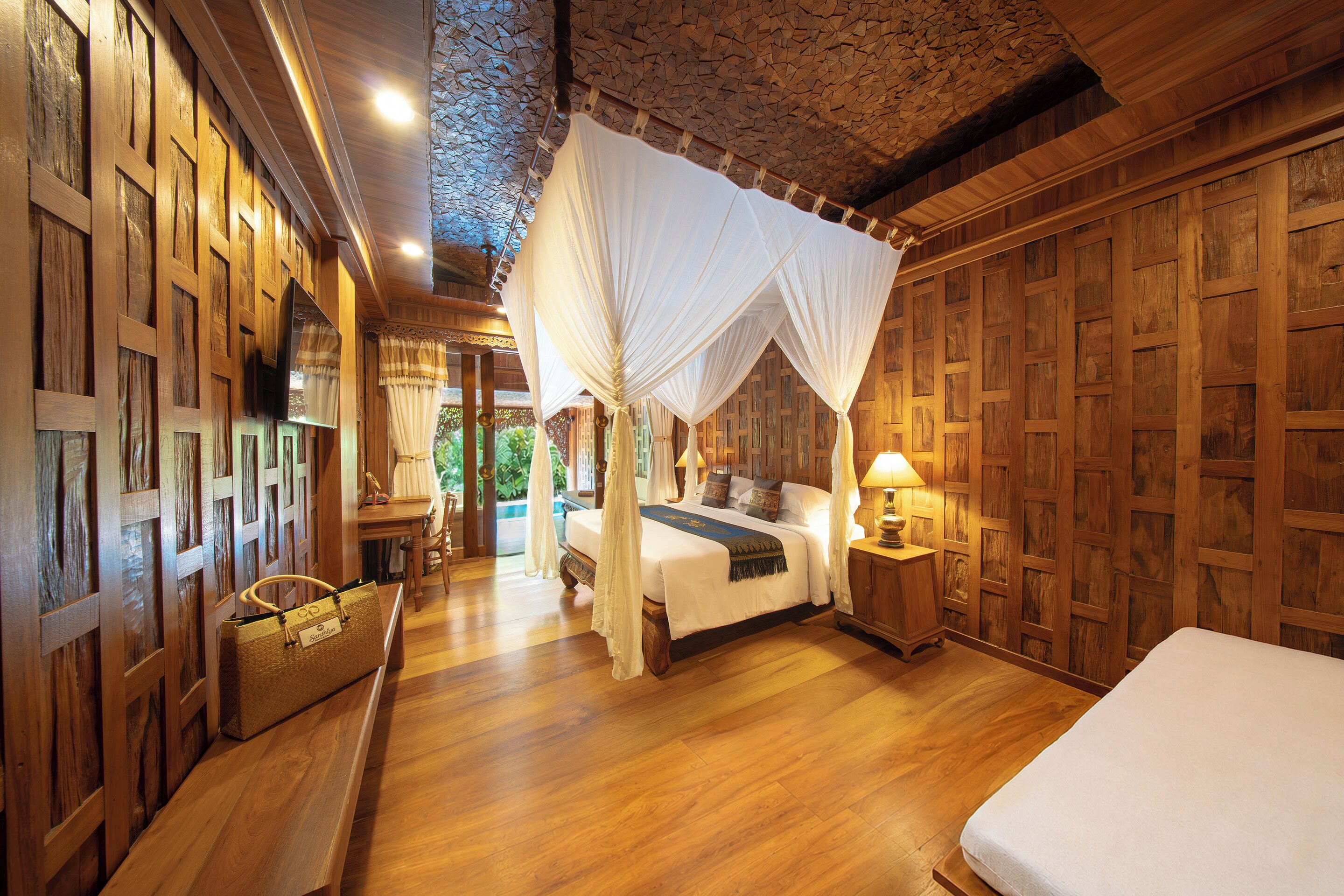 A room with a bed, a nightstand, a lamp, a wooden floor, and a ceiling with a wooden pattern.