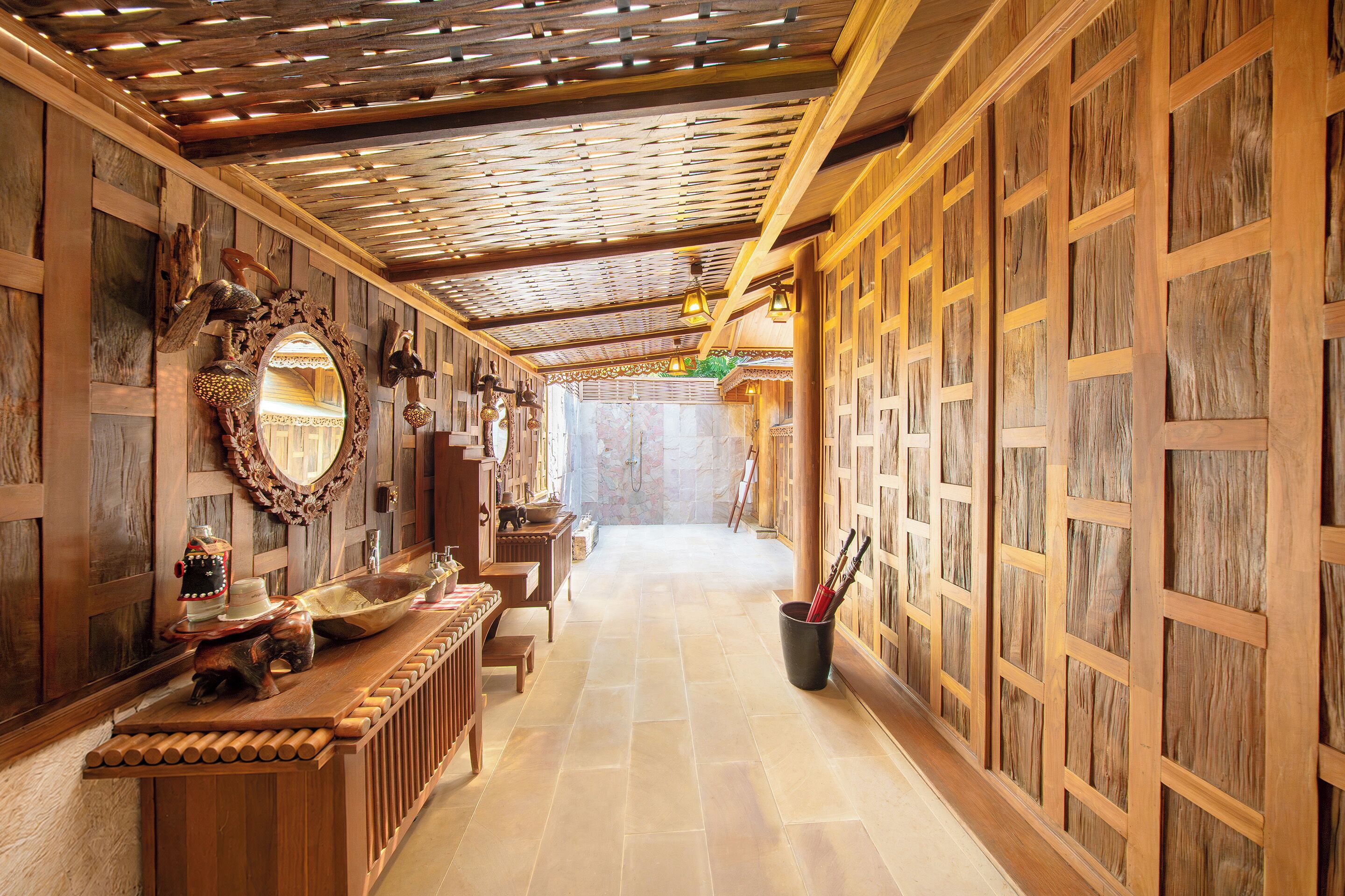 A hallway with wooden paneling and a slatted ceiling, leading to a bathroom with a stone wall and a shower.