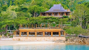 A beachfront property with a wooden structure, a stone wall, and a large house in the background.